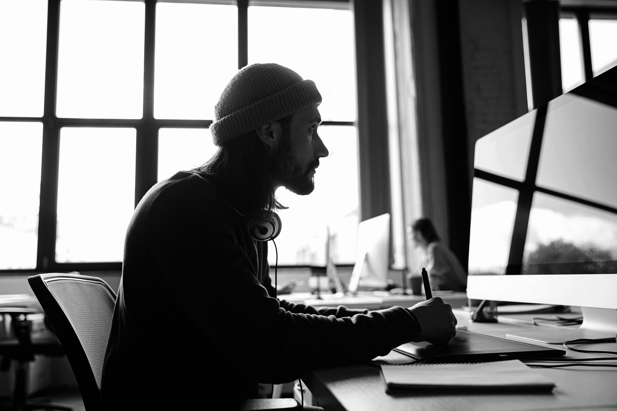 Foto eines Mitarbeiters am Computer, der Mann trägt eine Mütze und Kopfhörer